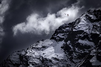 Two paragliders over snowy peak with dramatic clouds