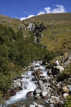 Hiker sitting by the mountain stream with waterfall in the Rofental
