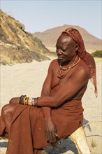 Himba woman resting at the bank of the dry river bed of the Hoarusib river