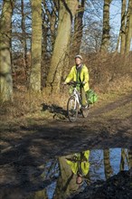 Woman cycling with e-bike over muddy forest path and through puddles