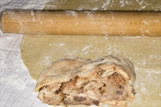 Rolling pin and a piece of apple strudel with sultanas lie on a strudel dough