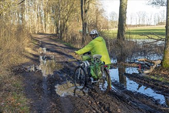 Woman cycling with e-bike over muddy forest path and through puddles