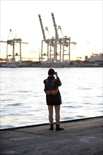 A person takes pictures of loading cranes at the Norderelbe in Altona