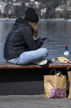 Teenager with smartphone eats take away food from McDonalds by the lake