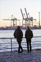 Two people in front of loading cranes at the Norderelbe in Altona