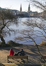 People on a park bench at the Inner Alster Lake with a view of the city skyline