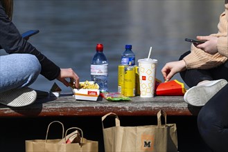 Teenagers with smartphones eat take away from McDonalds at the lake