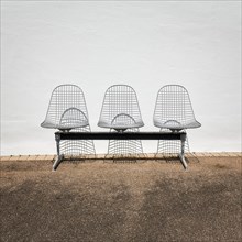 Three wire chairs in front of a white wall