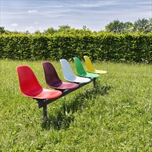 Five colourful plastic chairs in a meadow
