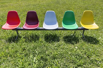 Five colourful plastic chairs in a meadow