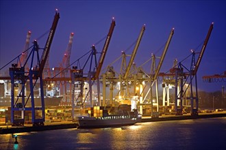 Loading cranes at the container terminal Burchardkai with a container ship in the evening