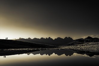 Salfainsee with reflection of the Kalkkoegel and mountaineers on mountain meadow at sunrise