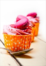 Fresh pink berry cream cupcake with macaroon on top over rustic wood table