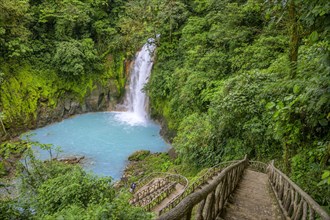 Many steps lead down to the waterfall with blue turquoise water of the Rio Celeste