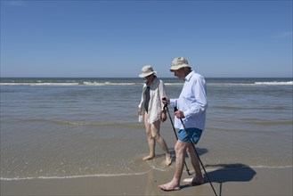 Elderly man accompanied by woman walking on the beach