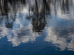 Trees and clouds in the blue sky reflected in the water of the Denstorf gravel pit near Braunschweig