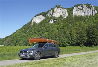Mercedes with cedar wood canoe on roof in front of rocks in the Danube valley