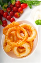 Golden deep fried onion rings served with mayonnaise dip and fresh vegetables oln background