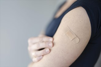 Arm of a woman with a plaster on her upper arm after vaccination
