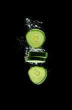 Sliced bio cucumber splashing water isolated on black background