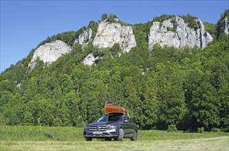 Mercedes with cedar wood canoe on roof in front of rocks in the Danube valley