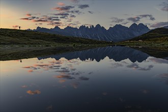Salfainsee with reflection of the Kalkkoegel and mountaineers on mountain meadow at sunrise