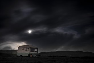 Old caravan in meadow under full moon