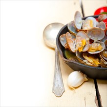 Fresh clams stewed on an iron skillet over wite rustic wood table