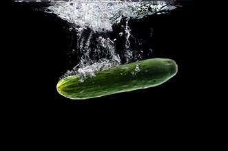 Whole bio cucumber sinking under water against black background