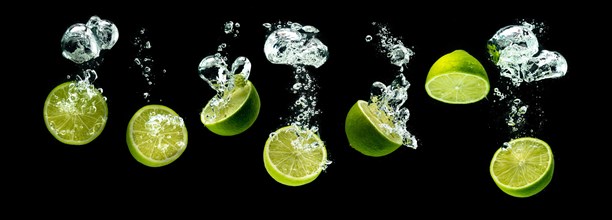 Bunch of lime fruits halves sinking with bubbles into water isolated against black background