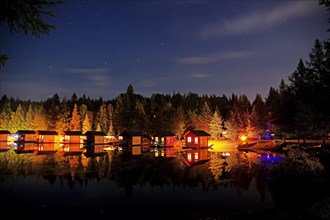 Small wooden holiday cabins at night on the shore of a lake