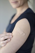 Arm of a woman with a plaster on her upper arm after vaccination