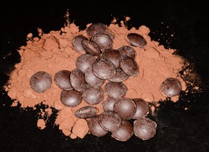 Dark couverture chocolate drops lying on cocoa powder