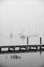 Empty bathing jetty with sailing boats in the morning mist