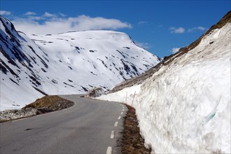 Road leads up along high snow walls and snowy mountains