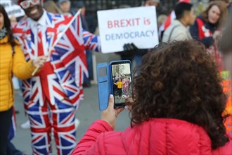 Woman taking photo of UK man in Union Jack suit with Brexit Democracy sign. Westminster