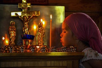 A girl blowing off a candle in a traditional wooden Russian Orthodox Church in Yuzhno-Sakhalinsk