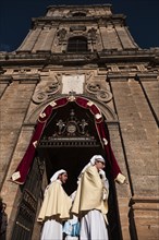 Two young members of a brotherhood dressed for Good Friday at the door of the Cathedral of Enna