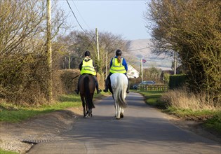 Two women riding horses along quiet country road