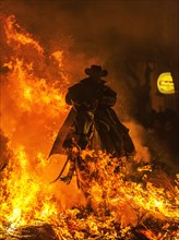 Arider with his horse jumping through a bonfire in an apocalyptic scene of Las Luminarias during the feast of St. Anthony held annually in the streets of the small mountain hamlet of San Bartolome de ...