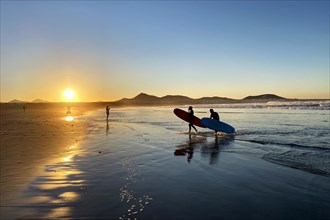 Surfers on Caleta de Famara beach at sunset