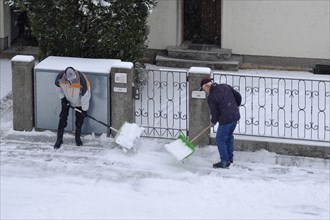 Two men clearing snow from the pavement