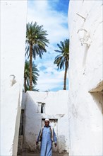 An elderly Berber man walking through the whitewashed buildings of Ghadmes