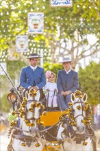 Two men and a young girl on a cart pulled by horses during the Feria de Abril in Seville