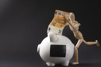 Piggy bank and a mannequin happily throwing a banknote into it