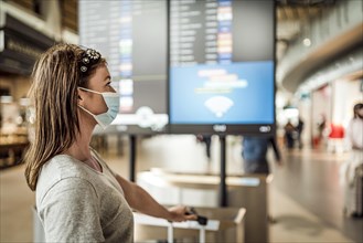 A young girl in mask waiting at the airport with flight information board as the background
