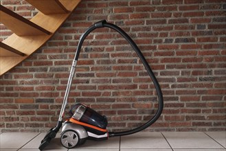 Vacuum cleaner under the stairs against the background of a brick wall