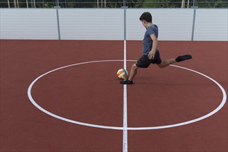 Boy kicks a ball in a football cage