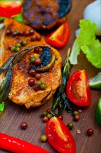 Wood fired hoven cooked chicken breast on wood board with herbs spices and vegetables