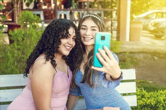 Two pretty girls sitting on a bench taking a selfie